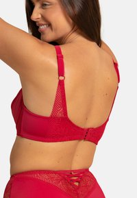 Soutien-gorge en dentelle rouge et satin avec bretelles réglables, fermeture à crochet et détails en dentelle florale au dos. Fini lisse avec accents texturés.