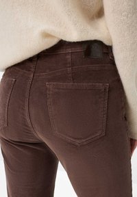 Ingrandimento di una persona che indossa pantaloni di velluto a coste marroni con tasche posteriori e un maglione di maglia crema inserito in vita.