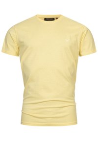 T-shirt en coton jaune avec un col rond et des manches courtes. Présente un petit logo blanc sur la partie gauche de la poitrine. Texture douce.