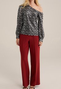 Černý a stříbrný vzorovaný top s odhalenými rameny a dlouhými rukávy, kombinovaný s červenými širokými kalhotami a černými sandály na řemínky.