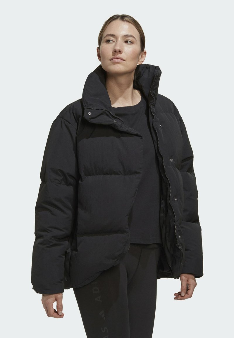 Schwarze Pufferjacke mit hohem Kragen, leicht lockerem Schnitt und sichtbaren Druckknöpfen, die ein strukturiertes, gestepptes Aussehen aufweist.