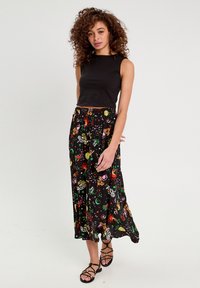 Top de tank noir raccourci associé à une longue jupe fluide ornée de motifs floraux et célestes colorés, fabriquée en tissu léger.