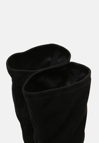 Black suede knee-high boots with soft texture, wide openings, and stitched detailing along the edges.