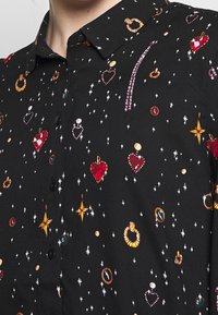 Camicetta nera con bottoni caratterizzata da un motivo di ornamenti colorati, cuori e stelle. Realizzata in un tessuto liscio con un design di colletto classico.