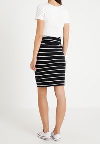 Svartvit randig blyertskjol, åtsittande design, bomullsblandat material, kombinerad med en vit kortärmad topp och vita sneakers.