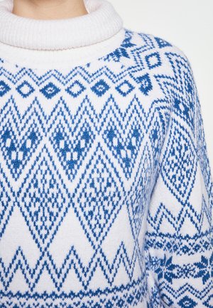 Witte trui met een hoge, geribbelde kraag, versierd met blauwe geometrische patronen, waaronder diamanten en zigzags, op een textuur gebreide stof.