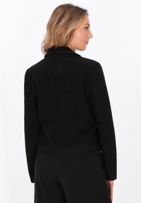 Giacca nera corta con maniche lunghe e colletto a punte. Realizzata in un tessuto texturizzato, presenta una silhouette aderente e cuciture pulite.