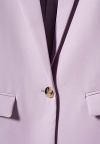 Blazer lilas en tissu lisse, avec des revers aiguisés, une fermeture simple bouton à motif marbré et deux poches plaquées à l'avant.