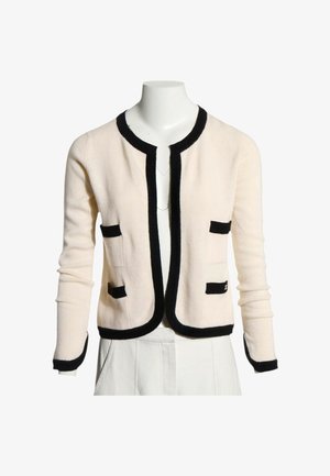 Cardigan crème à manches longues avec bordures noires le long des bords, des poches et des poignets, présenté sur un buste de mannequin blanc.