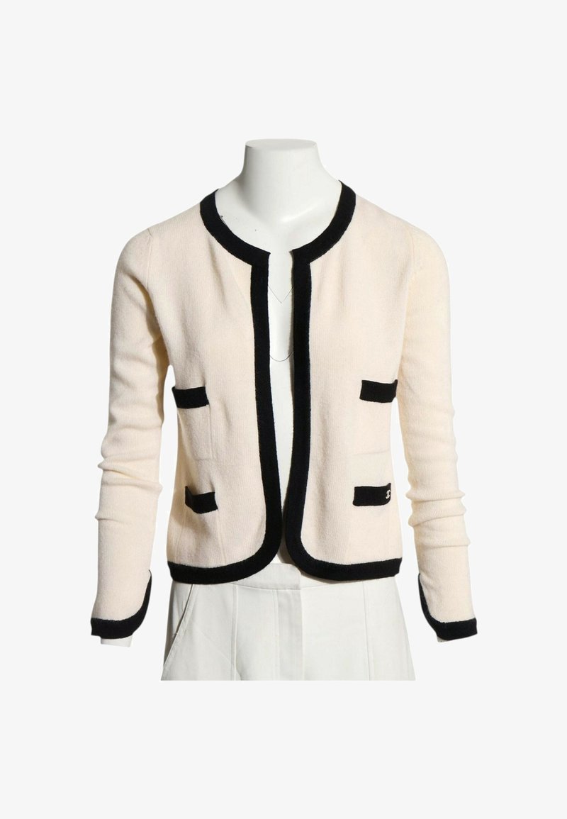 Cardigan crème à manches longues avec bordures noires le long des bords, des poches et des poignets, présenté sur un buste de mannequin blanc.