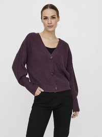 Chunky knit cardigan in dark purple, featuring a deep V-neck, three brown buttons, and loose sleeves; paired with slim black pants.