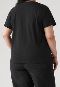 Person wearing a plain black short-sleeve t-shirt and black jeans, shown from the back against a plain light background.