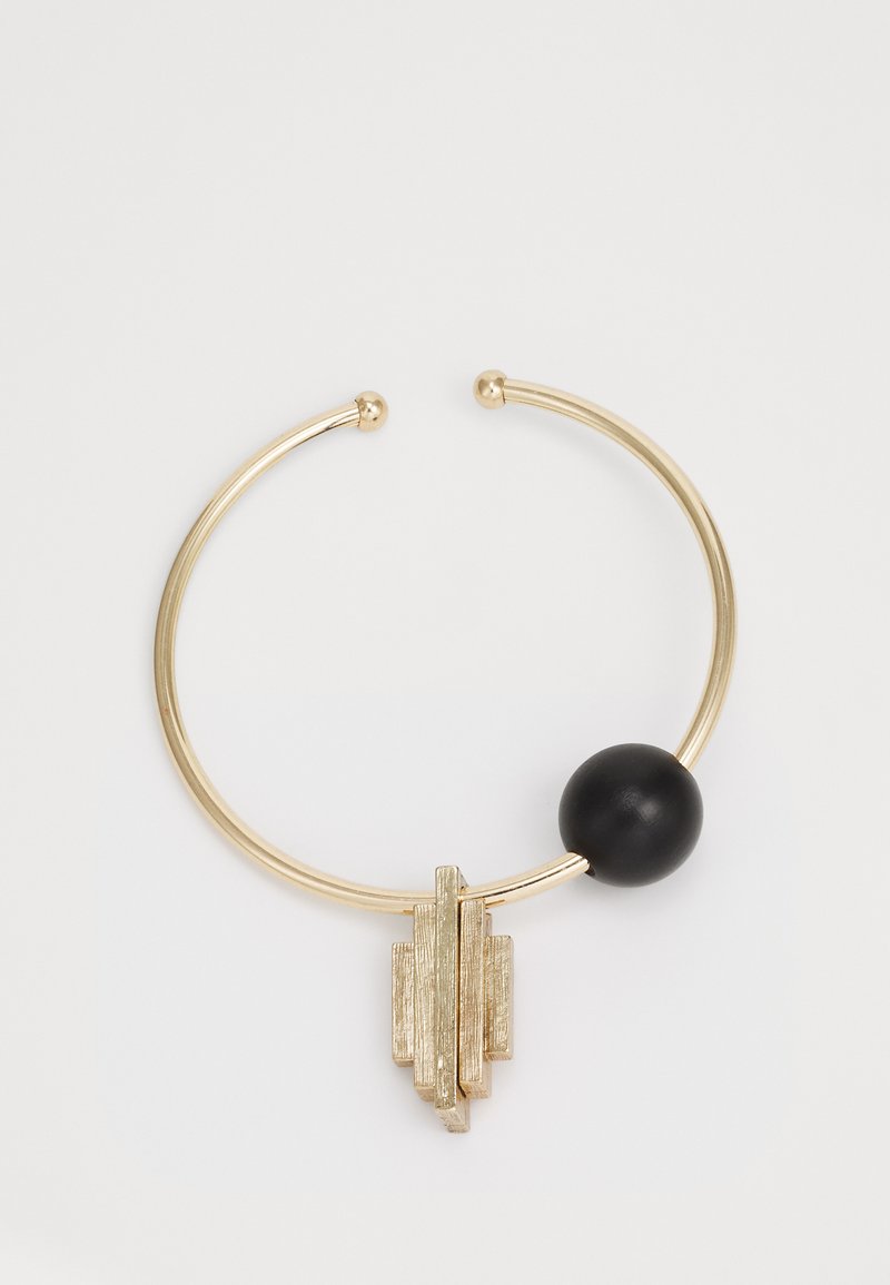 Guldfärgad metallarmband med en texturerad geometrisk design och en central svart sfärisk pärla. Slät yta och öppna ändar.