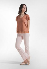 Verbrande oranje V-hals T-shirt met korte mouwen en een gelaagde zoom, gecombineerd met lichtroze uitlopende broek en zachte beige balletschoenen.