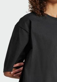 Černé oversized tričko vyrobené z bavlny, s krátkými rukávy a kulatým výstřihem. Hladký povrch s volným střihem.