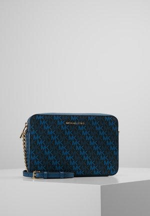 Michael Kors blauwe en zwarte crossbodytas met herhalend MK-logo patroon en gouden kettingriem op wit display oppervlak.