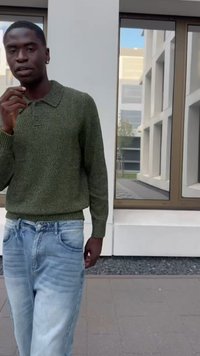 Zeleni pleteni pulover s polosek collarjem, v kombinaciji z svetlo modrimi denim hlačami. Tekstura se zdi mehka, barve pa so naravne in umirjene.