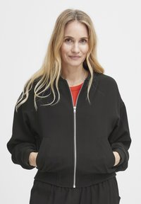 Čierna bomber bunda s doplnkovým zipsom, rebrovanými manžetami a bočnými vreckami, vyrobená z hladkého materiálu s voľným strihom.