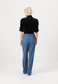 Svart fløyelsbluse med puffede ermer og nøkkelhullsrygg, parret med lyseblå mønstrede vide bukser med geometrisk design.