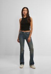 Črn skrajšan top na naramnice v kombinaciji z zbledelimi modrimi bootcut kavbojkami. Opozorljive podrobnosti vključujejo šive in gumbasto zapiranje. Bele superge zaokrožajo videz.