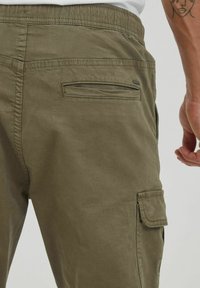 Khaki spodnie cargo z gładką teksturą, elastycznym pasem, bocznymi kieszeniami cargo oraz pojedynczą tylną kieszenią z klapką.