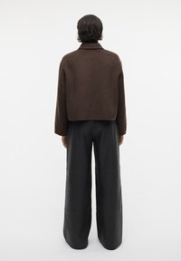 Bruine cropped jas met een gestructureerde kraag, gecombineerd met brede zwarte leren broek. Gladde textuur en minimalistisch ontwerp.