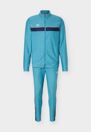 Φωτεινό γαλάζιο φόρμα Under Armour με ζακέτα φερμουάρ, ναυτικό οριζόντιο ρίγες στο στήθος και ταιριαστό στενό παντελόνι με πλαϊνές ρίγες.