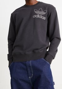 Černá mikina se žebrovanými manžetami a výstřihem, s bílým vyšívaným logem Adidas a designem tří pruhů na hrudi.