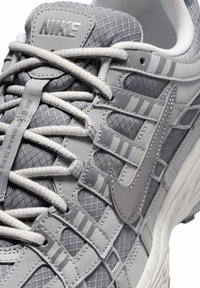 Szary sneaker marki Nike z białymi sznurowadłami, szczegółową siateczką i naszywanymi nakładkami, z logo Nike i charakterystycznym znakiem Swoosh na języku.