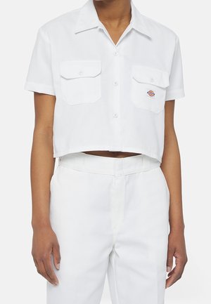 Person wearing white cropped short-sleeve button-up shirt with two chest pockets and matching high-waisted white pants.