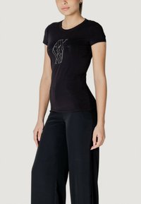 T-shirt nera in cotone a maniche corte con un design grafico argento sul davanti. Abbinata a pantaloni neri larghi.