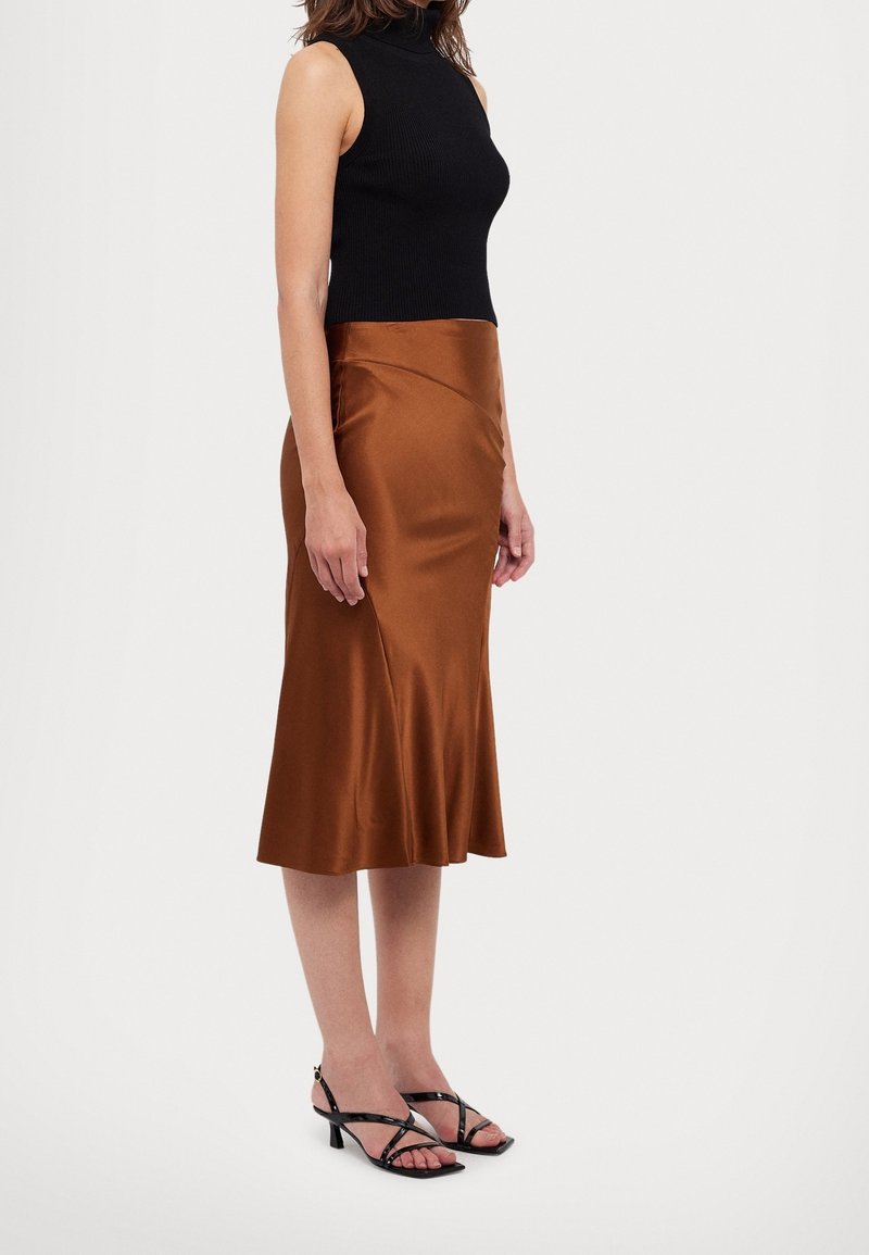 Top sin mangas de canalé negro, combinado con una falda midi de satén marrón chocolate, que presenta un dobladillo acampanado y un sutil detalle lateral. Sandalias negras de tiras.