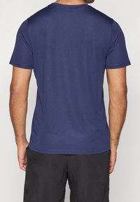 Modré tričko s krátkým rukávem, ribbovanou texturou, kulatým výstřihem a čistým lemem. Zadní strana má hladký design bez viditelných označení.