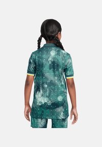 Completo sportivo verde con un design testurizzato e a motivi. La maglia presenta un colletto e accenti gialli sulle maniche. I pantaloni corti sono abbinati alla parte superiore.