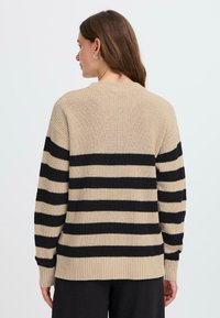 Maglione a strisce beige e nero realizzato in tessuto knit. Presenta un bordo e polsini a coste, con una vestibilità rilassata e un classico collo rotondo.
