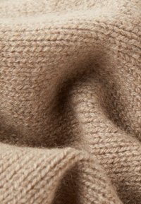 Beżowa dzianina o miękkiej, fakturowanej powierzchni. Charakteryzuje się luźnym splotem i subtelnym wzorem, oferując przytulny wygląd i ciepło.