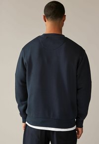 Felpa blu navy con scollatura rotonda, polsini e orlo a costine. Tessuto liscio, vestibilità comoda e design semplice senza decorazioni.