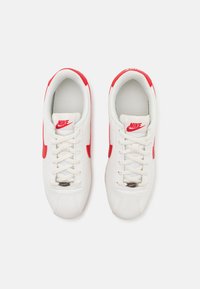 Weiße Sportschuhe mit roten Akzenten und Nike-Logo. Verfügt über ein glattes Lederoberteil, runde Zehenpartie und ein traditionelles Schnürsystem.