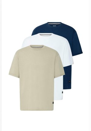 Mann steht und trägt ein marineblaues T-Shirt, hellblaue kniehohe Jeansshorts, weiße Socken und schwarze Turnschuhe mit weißen Streifen.