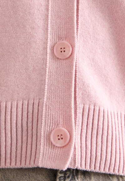 Roze cardigan met een geribbelde zoom en knoopsluiting, gemaakt van zachte stof. Opvallende ronde, roze knopen versterken het ontwerp.