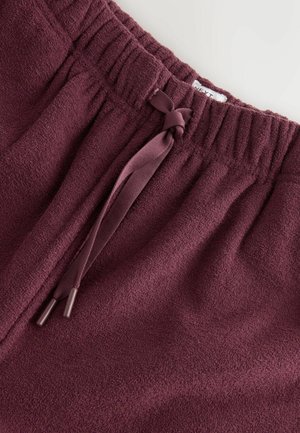 Burgundy fleece pants with an elastic waistband, featuring a drawstring tie. Soft texture with ribbed detailing at the waistband.
