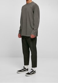 Chemise grise à manches longues avec un ourlet légèrement effiloché, associée à un pantalon texturé sombre et des baskets noires Vans avec des lacets blancs et des chaussettes.