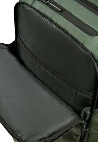 Mochila verde y negra abierta para mostrar el compartimento acolchado para laptop y el bolsillo interior con cremallera de tela con patrón de diamantes.
