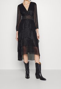 Svart lager-på-lager klänning med lång ärm, texturerad tyg och djup V-ringning. Kombinerad med knähöga svarta läderstövlar.