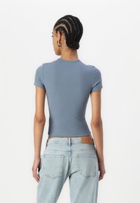 Light blue, ribbed short-sleeve top with a fitted design. Worn with light denim jeans featuring a leather label on the back waistband.