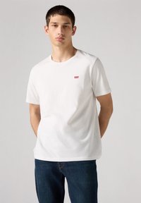 Witte katoenen T-shirt met korte mouwen, ronde hals en een klein rood Levi's-logo op de linkerborst. Draagt met blauwe denim jeans.