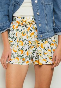 White shorts with a lemon and leaf pattern, featuring a gathered waist and tie detail, paired with a blue denim jacket.