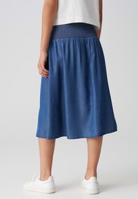 Denim A-linje nederdel med smocket talje, midt på læggen, i en ensfarvet mørkeblå farve, med en glat tekstur og syet kant.