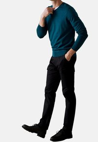 Maglione turchese con maniche lunghe, abbinato a pantaloni cargo neri e scarpe nere. Texture liscia, design aderente e dettagli sottili.