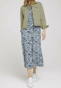 Kevyt oliivinvihreä takki, kukallinen sinivalkoinen maksimekko ja valkoiset tennarit. Mekossa on väljä istuvuus ja pyöreä kaula-aukko.